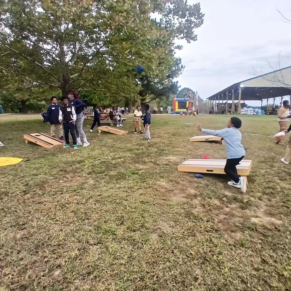 Kids playing cornhole on the grass under a shade tree