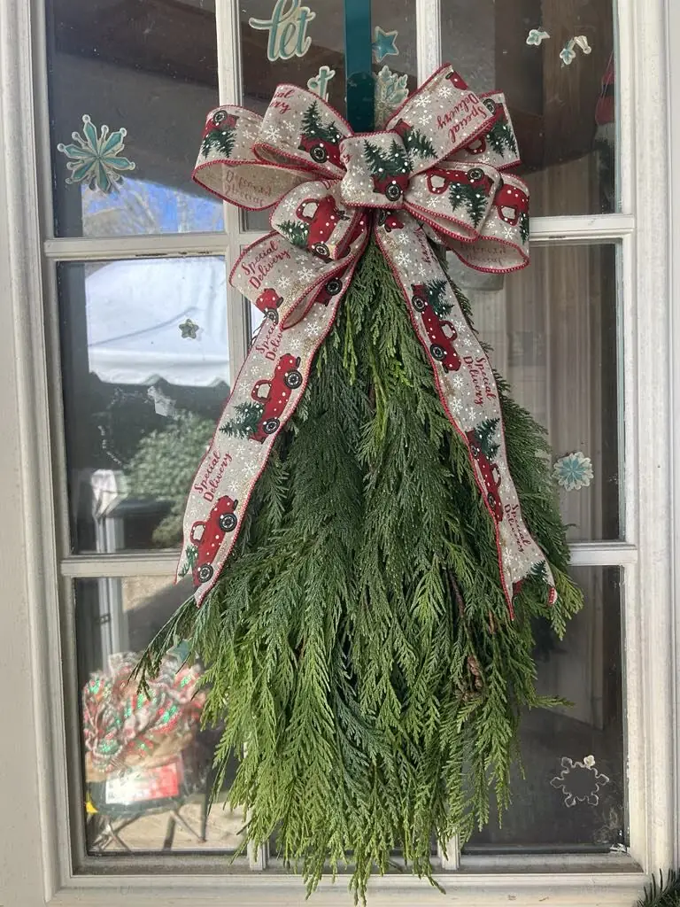 A garland swag with a red ribbon bow hanging on a door