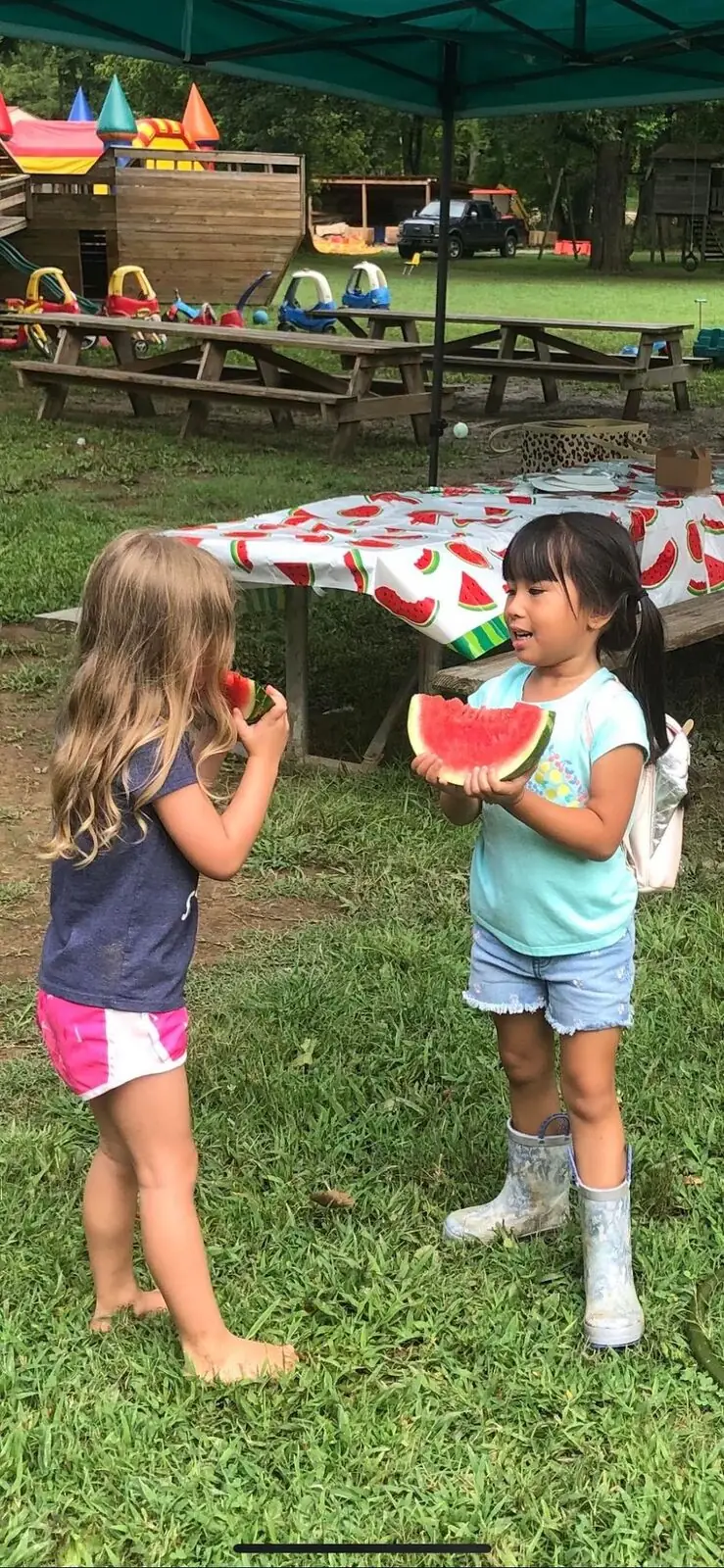 Two girls eating watermelon under a canopy